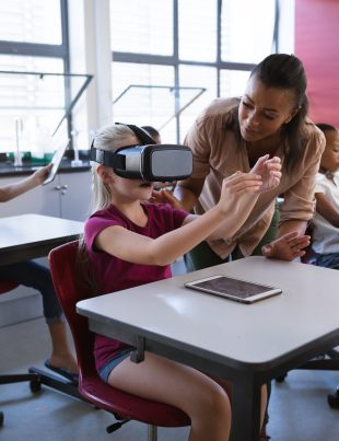 African american female teacher teaching caucasian girl to use vr headset in the class at school